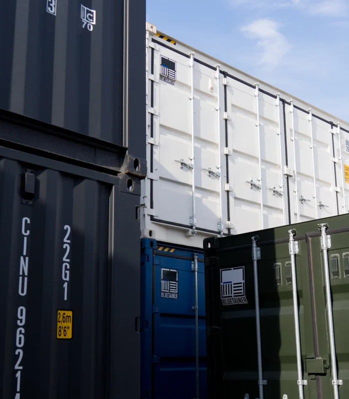 Vue détaillée d’un stock de conteneurs maritimes 20 pieds, empilés et prêts pour la transformation modulaire chez Bluetainer. Les unités bleues, grises et beiges illustrent la diversité disponible pour la construction et l’up‑cycling industriel.